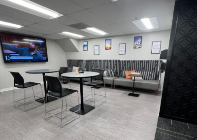 Lounge space featuring chairs, small, round high tables, and TV from Eastcastle Place senior living facility