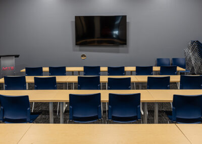 Straight on view of large meeting room space featuring TV and four rows of tables and chairs