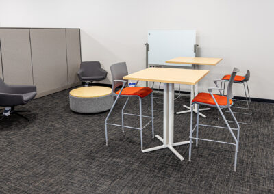 Small collaborative space featuring high tables, chairs, a coffee table, and white board at Westbrook MTE Tenant Buildout