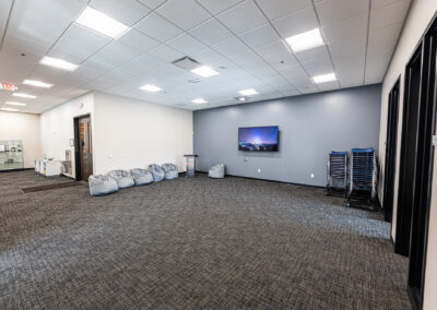 Empty meeting room space at Westbrook MTE Tenant Buildout featuring a mounted TV on a wall and an assortment of chairs stacked against a wall