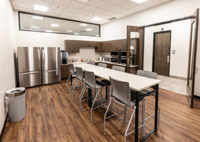 Kitchen space at Westbrook MTE Tenant Buildout featuring long high table, chairs, two refrigerators, cabinets, and microwaves