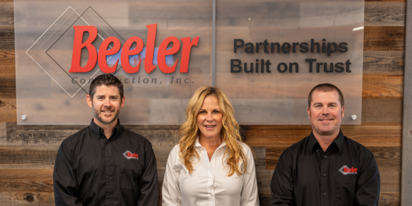 Dave, Kim and Chad smiling next to Beeler logo inside building